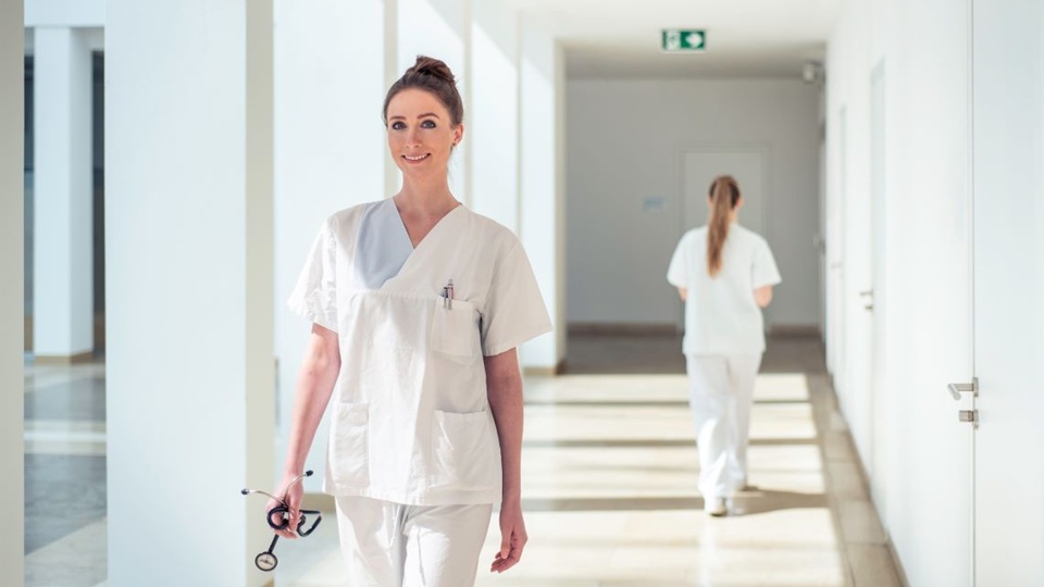 Eine Frau in weißer Pflegebekleidung auf einem sonnigen Gang