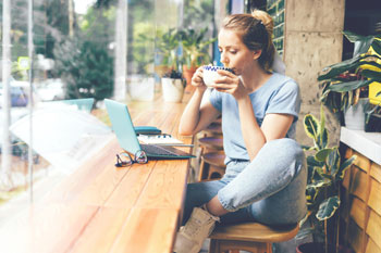Eine junge Frau lernt für ihr Fernstudium und trinkt eine Tasse Kaffee