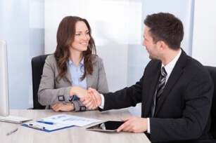 Eine Frau beim Bewerbungsgespräch mit einem Mann, beide schütteln sich die Hände