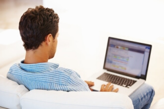 Ein Mann sitzt an einem Laptop und recherchiert verschiedene Anbieter eines Fernstudiums