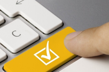 Ein Zeigefinger drückt auf die linke Shift-Taste der Tastatur, welche gelb hervorgehoben und mit einem weißen Haken versehen ist