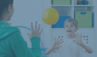 Eine Ergotherapeutin wirft einem Jungen einen Ball zu.