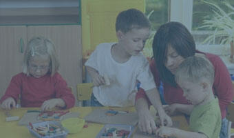 Eine Pädagogin spielt mit Kindern an einem Tisch.