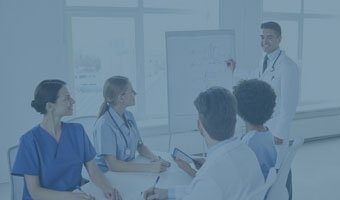 Ein Arzt präsentiert etwas an einem Whiteboard vor vier anderen Ärzten in einem Konferenzraum.
