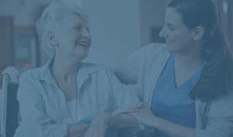 Pflegewissenschaftlerin sitzt mit einer älteren Dame zusammen, sie unterhalten sich angeregt