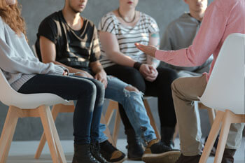 Eine Gruppe Jugendlicher sitzt mit einem Sozialarbeiter zusammen und spricht über Probleme