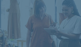 Verkäuferin zeigt Kundin über das Tablet, wie diese ihre Klamotten auch im Online-Shop erwerben kann.